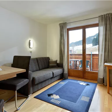 A cozy living room with a balcony and a view of the mountains. There is a sofa, a table, and a television.