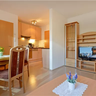 A modern apartment with a kitchen and a living area. The room is bright and friendly, with a dining table and a television.