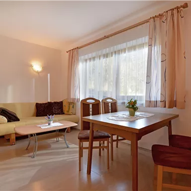 A bright living room with a comfortable sofa and a dining table. The large windows let in plenty of daylight.