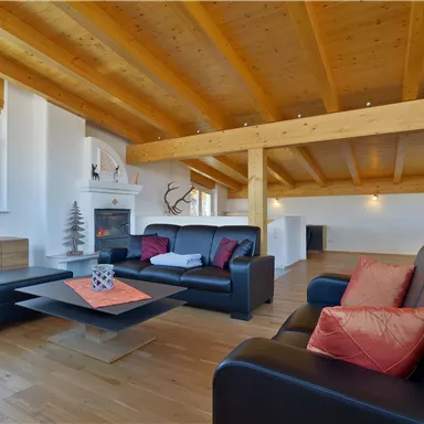 Ein modernes Wohnzimmer mit Holzdecken und großen Fenstern. Schwarze Sofas und eine stilvolle Kaffeetisch-Arrangierung schaffen eine einladende Atmosphäre.