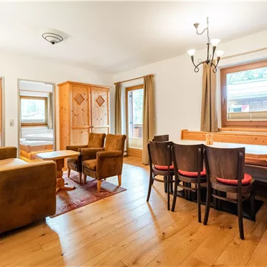 Ein helles Wohnzimmer mit bequemen Möbeln und einem Essbereich. Die Wände sind in neutralen Farben gehalten, und große Fenster sorgen für viel Tageslicht.