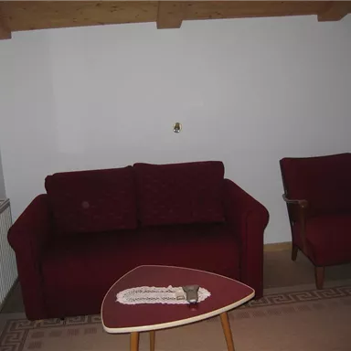 A living room with a red sofa and a cozy armchair. A small table stands in the middle on a rug.