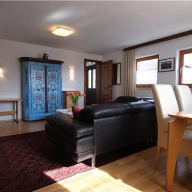 Ein gemütliches Wohnzimmer mit einem schwarzen Sofa und einem blauen Schrank. Der Raum ist hell und einladend, mit einem Esstisch und Stühlen.