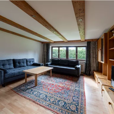 A cozy living room with two sofas, a table, and a rug. Large windows let in plenty of daylight.