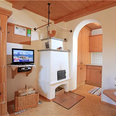 Ein gemütlicher Wohnraum mit Holzdetails und einem Fernseher. Der Raum hat eine offene Küche und viel natürliche Beleuchtung.