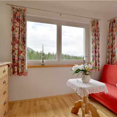 A cozy living space with a red sofa and a small table. The large windows offer a view of nature.