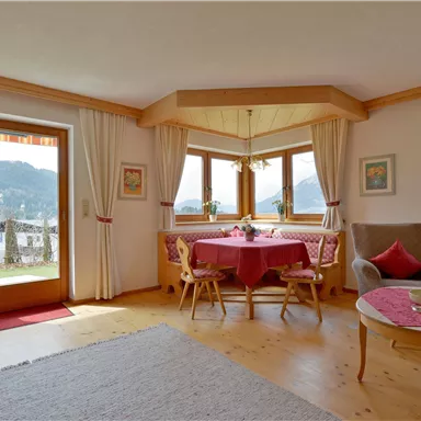 Ein gemütliches Wohnzimmer mit einem runden Esstisch und Blick auf die Berge. Große Fenster lassen viel Licht herein und vermitteln eine einladende Atmosphäre.