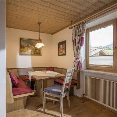 A cozy dining area with a table and chairs. Through the windows, one looks out onto a green landscape.
