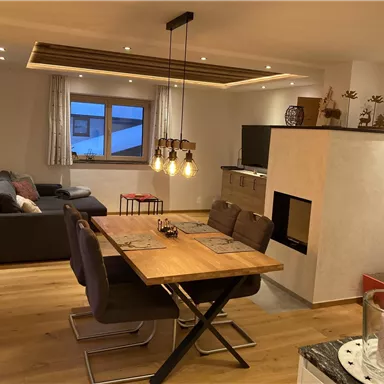 Ein modernes Wohnzimmer mit einem Essbereich und einer gemütlichen Atmosphäre. Große Fenster sorgen für viel Licht und einen Blick nach draußen.