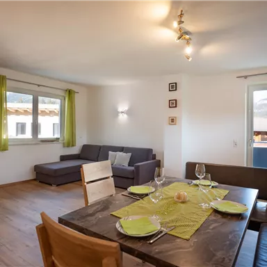 A cozy living room with a seating area and a dining table. The walls are light, and green curtains create a friendly atmosphere.