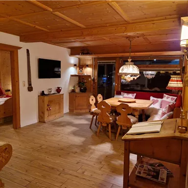 Ein gemütlicher Raum mit einem Holztisch und Stühlen. Die Wände sind aus Holz, und es gibt eine warme Beleuchtung.