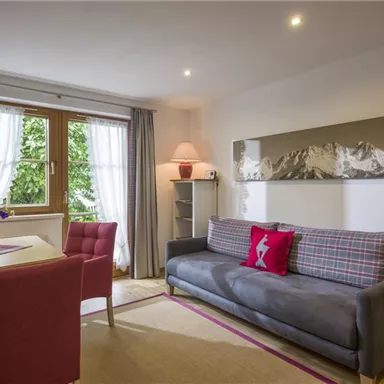 A cozy living area with a gray sofa and red chairs. The window lets in plenty of daylight and offers a view of nature.