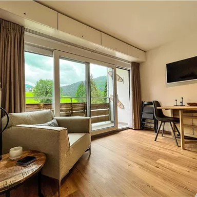 Ein gemütlicher Wohnbereich mit einem bequemen Sofa und einem kleinen Tisch. Große Fenster ermöglichen einen Blick auf die grüne Landschaft draußen.