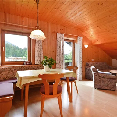 Ein gemütliches Zimmer mit Holzverkleidung und großen Fenstern. Es gibt einen Esstisch und bequeme Sitzgelegenheiten.