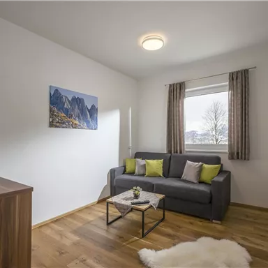 A modern living room with wooden flooring and a comfortable sofa. The room has large windows and is bright with a beautiful view.