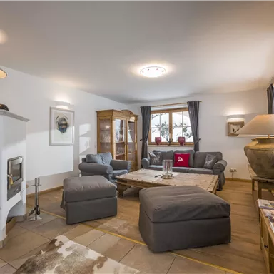 Ein gemütliches Wohnzimmer mit bequemen Sofas und einem Holztisch. Das Zimmer hat große Fenster und eine warme, einladende Atmosphäre.