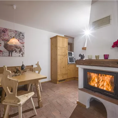 A cozy living space with a wood stove and a dining table. The walls are decorated with pictures, and the room has a warm, inviting atmosphere.