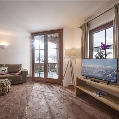 An inviting living room with a large window that lets in plenty of light. The furnishings include a comfortable couch, a television, and a decorative table.