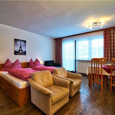 Ein gemütliches Hotelzimmer mit zwei Einzelbetten und bequemen Sesseln. Große Fenster sorgen für viel Tageslicht und eine angenehme Atmosphäre.