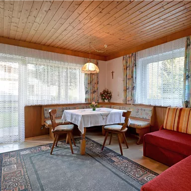 Ein gemütlicher Essbereich mit einem weißen Tisch und Stühlen. Das Zimmer hat helle Fenster und warme Holzelemente.