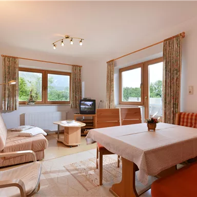 A cozy living room with a table and several seating options. Large windows let in plenty of daylight and offer a view of the surroundings.