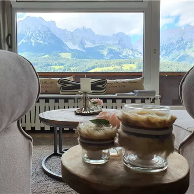 A cozy room with a view of the mountains. On the table are decorative glasses and a candle.