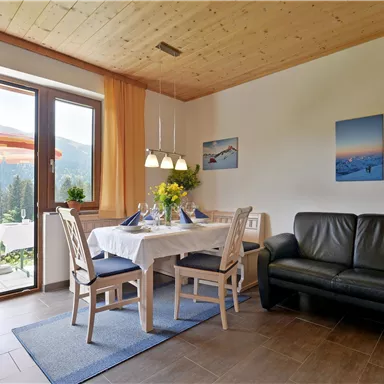 Ein gemütlicher Wohnraum mit einem Esstisch und Stühlen. Große Fenster lassen viel natürliches Licht herein und bieten einen Blick auf die Umgebung.