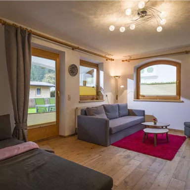 A modern living room with comfortable sofas and a small table. Large windows provide plenty of natural light and a view of the surroundings.