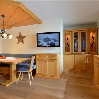 Ein gemütlicher Essbereich mit Holzmöbeln und einer abgerundeten Decke. An der Wand hängt ein Fernseher, daneben steht ein Vitrinenschrank.