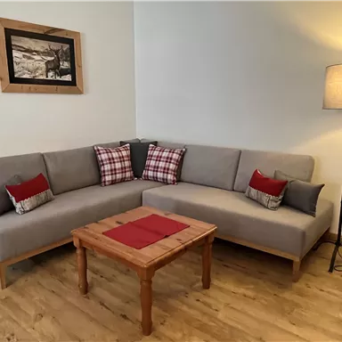 A cozy living room with a gray sofa and colorful cushions. A wooden coffee table stands in the middle, and beside the sofa is a floor lamp.