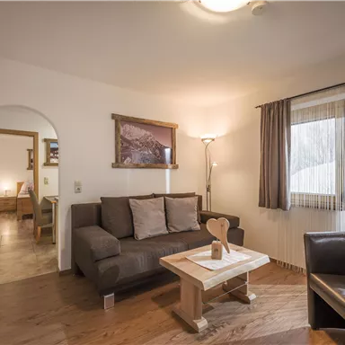 A cozy living room with a sofa and a table. Large windows let in plenty of light and create an inviting atmosphere.