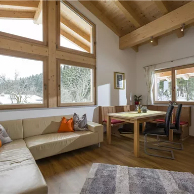 Ein modernes Wohnzimmer mit Holzdecken und großen Fenstern. Es gibt ein gemütliches Sofa, einen Essbereich und einen Teppich auf dem Boden.