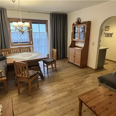 A cozy living space with wooden furniture and a dining table. Large windows provide plenty of light.