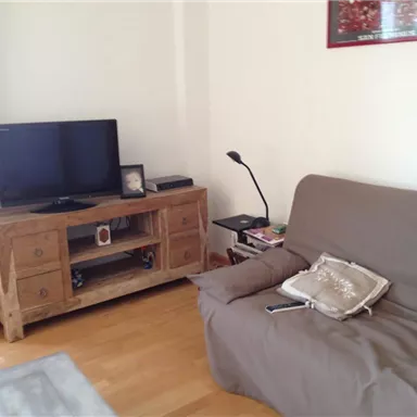 A cozy living room with a sofa and a wooden cabinet. A television stands on the cabinet, and a lamp illuminates the room.