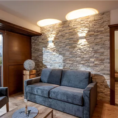 A modern living room with a gray couch and a decorative table. The room has a stone wall and large windows with a view of the mountains.