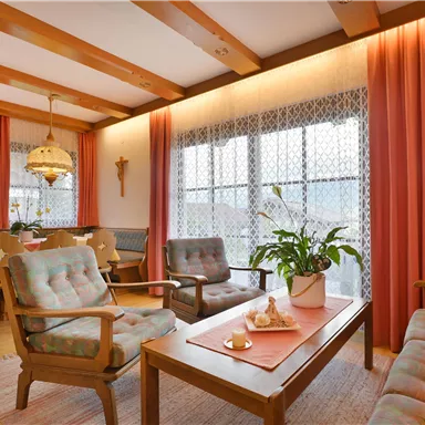 Ein gemütliches Wohnzimmer mit Holzbalken und roten Vorhängen. Es gibt bequeme Möbel und eine Pflanze auf dem Tisch.