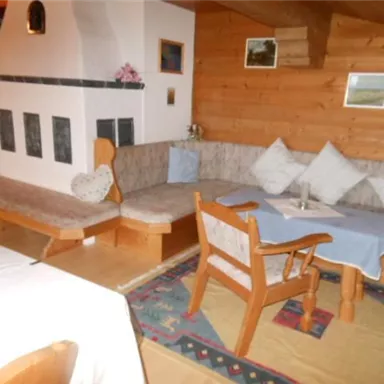 Ein gemütlicher Wohnbereich mit Holzverkleidungen und einer Sitzecke. Ein Tisch mit blauer Tischdecke und einladenden Kissen sorgt für eine warme Atmosphäre.