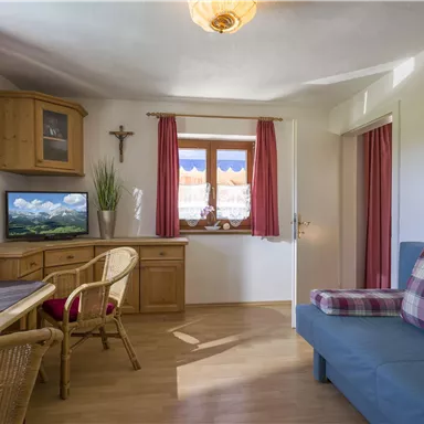 Ein gemütliches Wohnzimmer mit einer blauen Couch und einem Holztisch. Die Fenster sind mit roten Vorhängen dekoriert und bieten einen Blick auf die Landschaft.