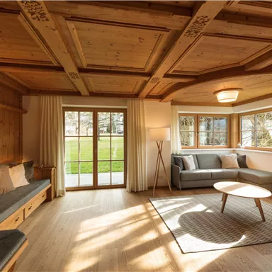A cozy living room with wooden walls and a large front window. The decor is modern and inviting, featuring a sofa and a coffee table.