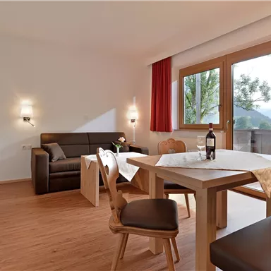 Eine helle Wohnung mit modernen Möbeln und einem großen Fenster. Der Tisch ist hübsch gedeckt und eine Flasche Wein steht bereit.