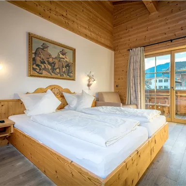 Ein gemütliches Schlafzimmer mit Holzwänden und großen Fenstern. Das Zimmer verfügt über ein Doppelbett und einen Balkon mit Blick auf die Berge.