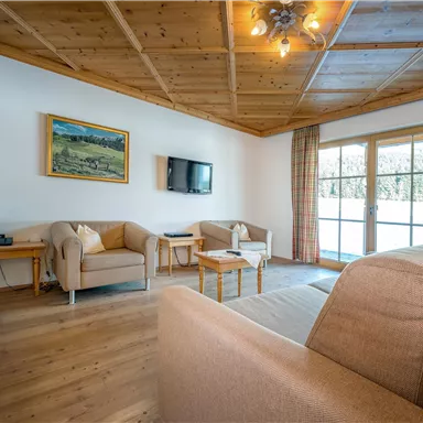 Ein gemütlicher Wohnbereich mit einem hellen Sofa und bequemen Sesseln. Große Fenster sorgen für viel Tageslicht und einen Ausblick nach draußen.