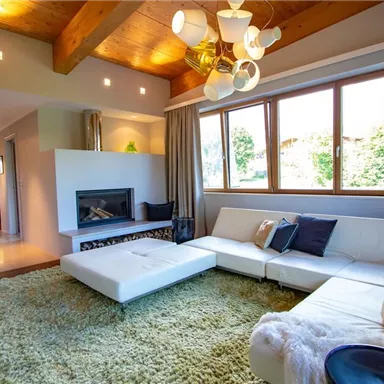 A modern living room with a white sofa and a cozy rug. Large windows let in plenty of light and offer a view of nature.
