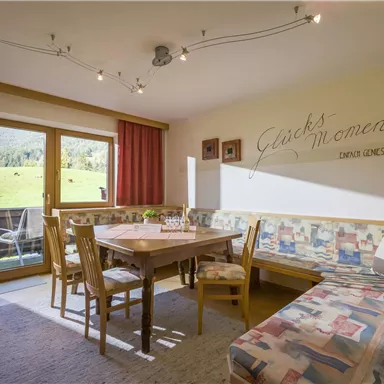 A cozy dining area with a wooden table and chairs. Large windows offer a view of the green landscape.