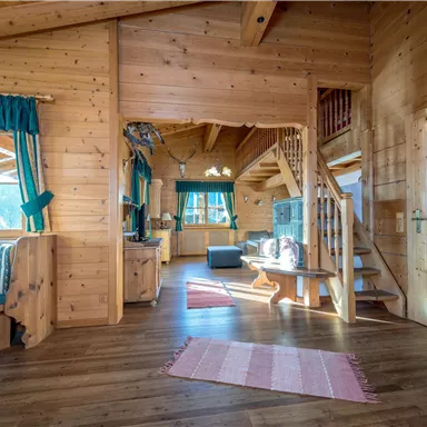 Ein gemütlicher Wohnraum mit Holzverkleidung und hellem Licht. Die Einrichtung ist rustikal, mit einer Treppe und großen Fenstern.