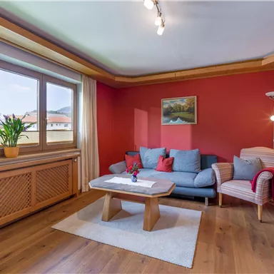 Ein gemütliches Wohnzimmer mit roten Wänden und großen Fenstern. Ein Holzkaffee-Tisch und eine bequeme Couch bieten einen einladenden Raum zum Entspannen.