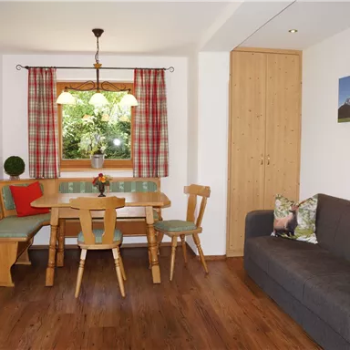 Ein gemütlicher Wohnraum mit einem Essbereich und einem Sofa. Große Fenster lassen viel Licht herein und bieten einen Blick ins Grüne.