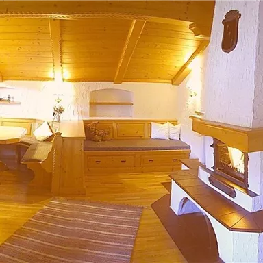 A cozy living room with wood paneling and a fireplace. There is a dining area and a relaxed seating corner.