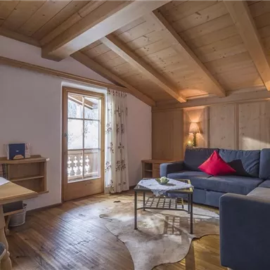 Eine gemütliche Wohnzimmerumgebung mit Holzwänden und einem schrägen Dach. Ein Sofa mit roten Kissen bietet Platz zum Entspannen, während ein schöner Tisch und ein Fenster für Licht sorgen.