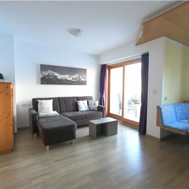 Ein modernes Wohnzimmer mit einer gemütlichen Couch und einem Tisch. Große Fenster lassen viel Licht herein und bieten einen Blick nach draußen.